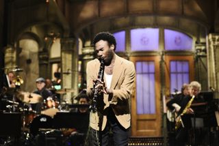 Donald Glover playing an instrument and wearing a tan suit on snl