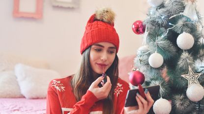 woman applying makeup in front of Christmas tree