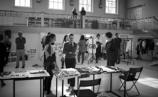 Black and white image of people looking at designs and fabrics laid out onto tables