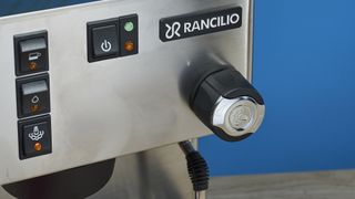 Rancilio Silvia in Stainless steel on a wooden worktop with a blue wall in the background.