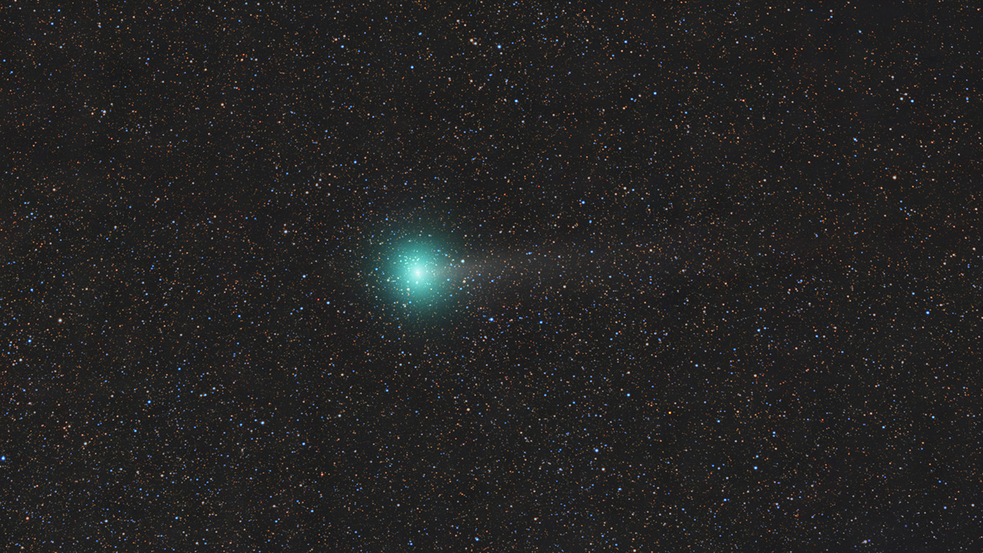 The bright central nucleus of a wandering comet is pictured glowing against the starfield beyond, with a faint tail extending away to the right of the image.
