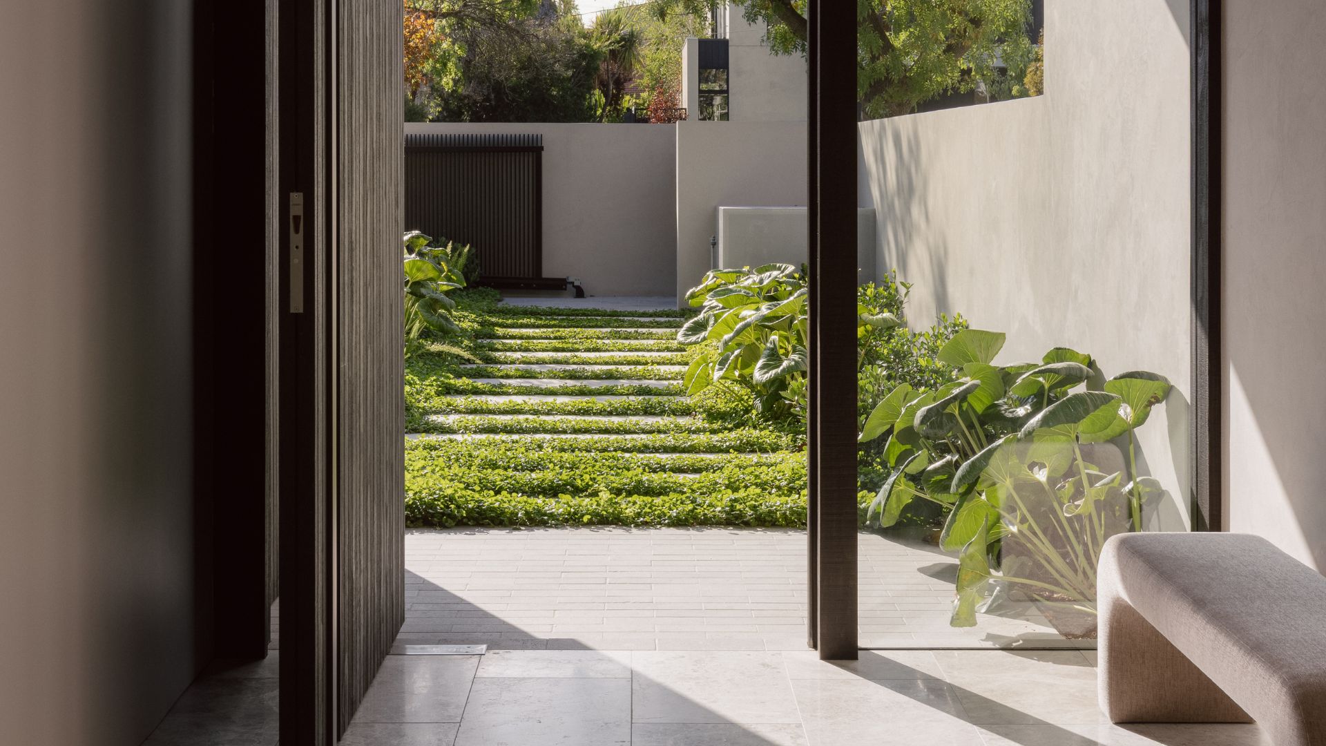 An entryway with a wooden door and curved bench leading to a front garden with ground cover and lush borders