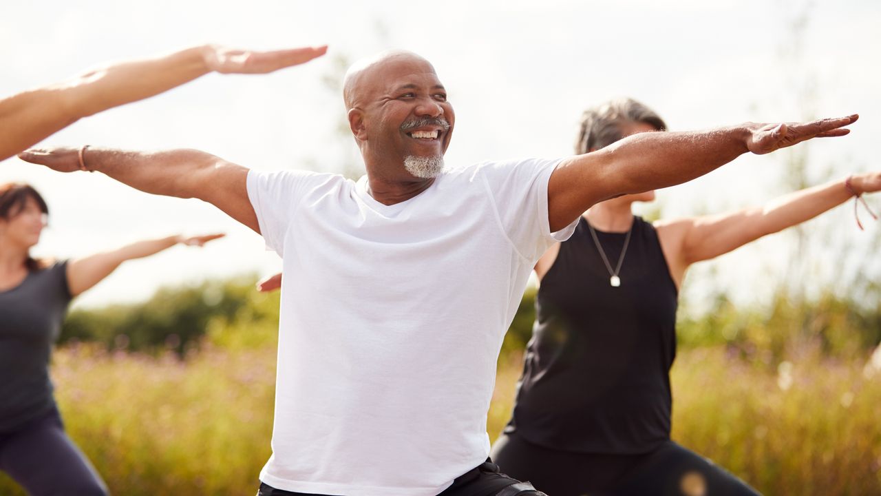 Group of people practicing yoga outdoors holding warrior two pose