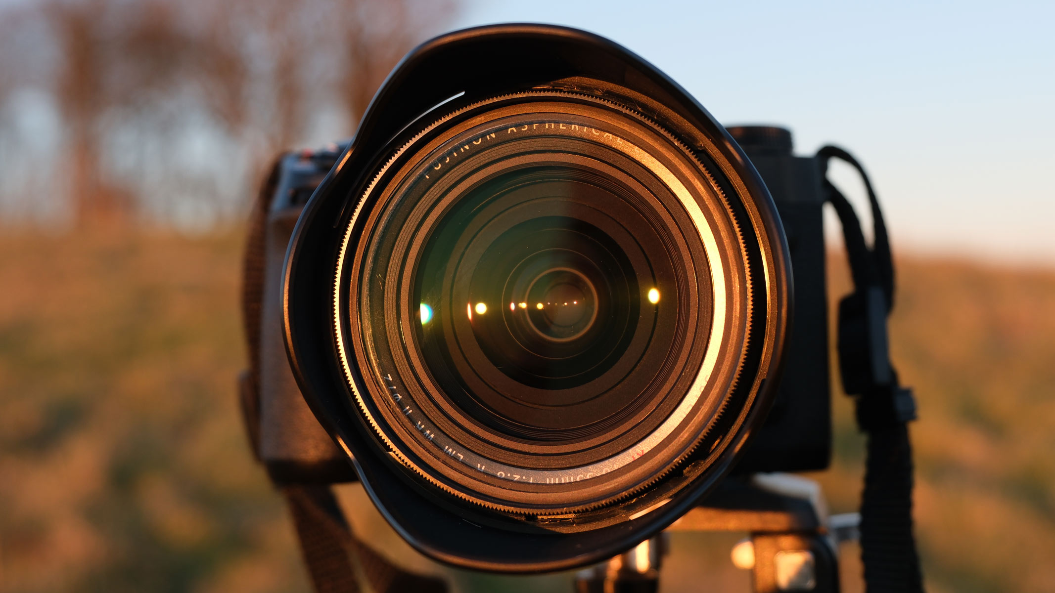 A head-on view of the Fujifilm X-H2 with the Fujifilm XF 16-55mm f/2.8 LM WR II lens attached and a field in the background