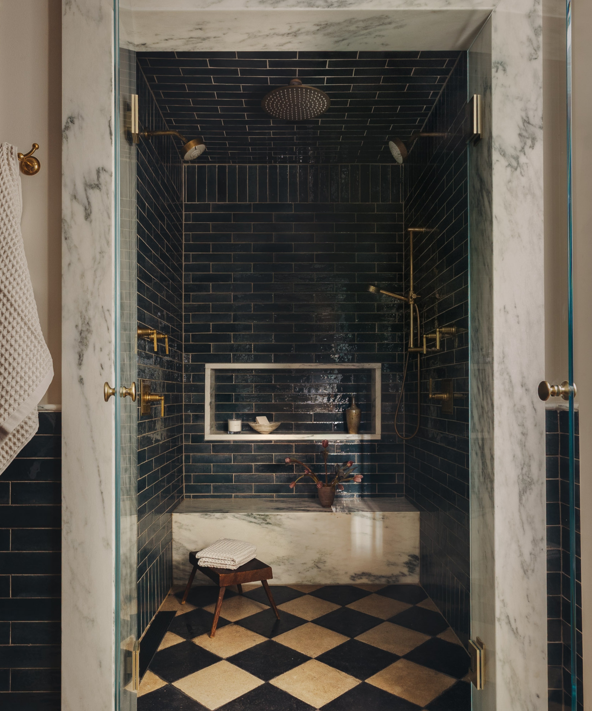 A moody shower room with dark green wall tiles, black and white checkerboard floor tiles, and a marble shower bench to match the ceiling and trim around the shower door