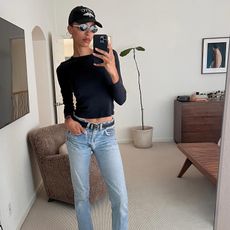 L.A. woman takes a selfie in a baseball cap, straight leg jeans, black long sleeve t-shirt and sunglasses