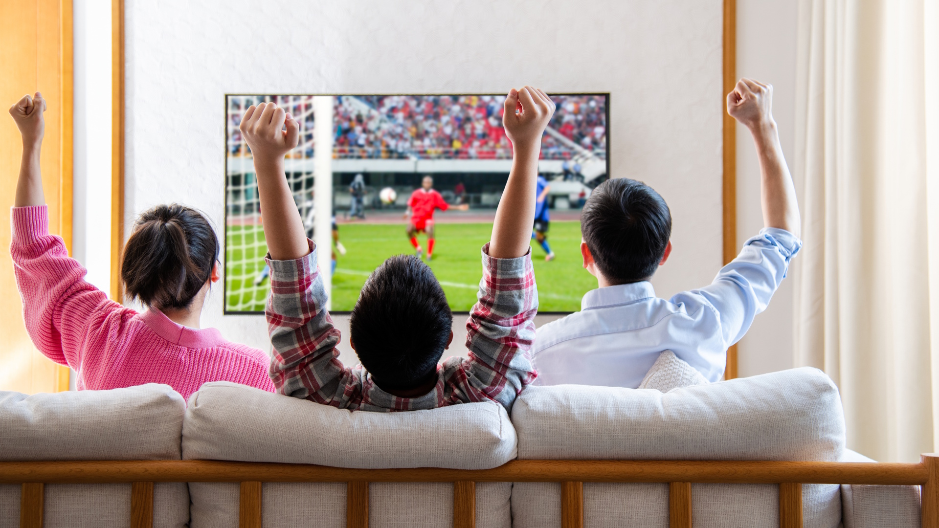 Family watching television and cheering soccer game on TV together in their living room.