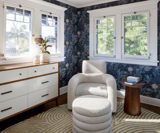 nursery with white easy chair and white footstool with blue wallpaper and windows on both sides