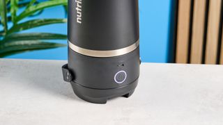 the Nutribullet Flip with a black insulated tumbler and a portable battery-powered blade photographed with a blue background. The tumbler has a carry strap and a sippy lid you can interchange, and an on/off button on the base.