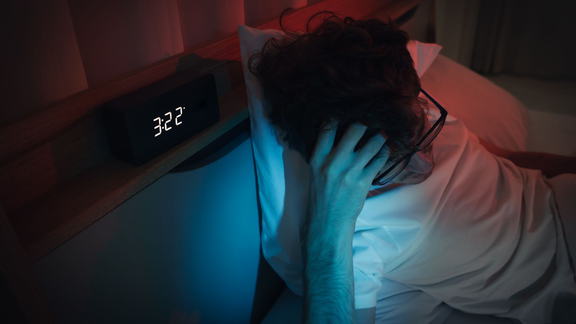 A man sits up in bed with his hand on his head shortly after 3 am in the morning.