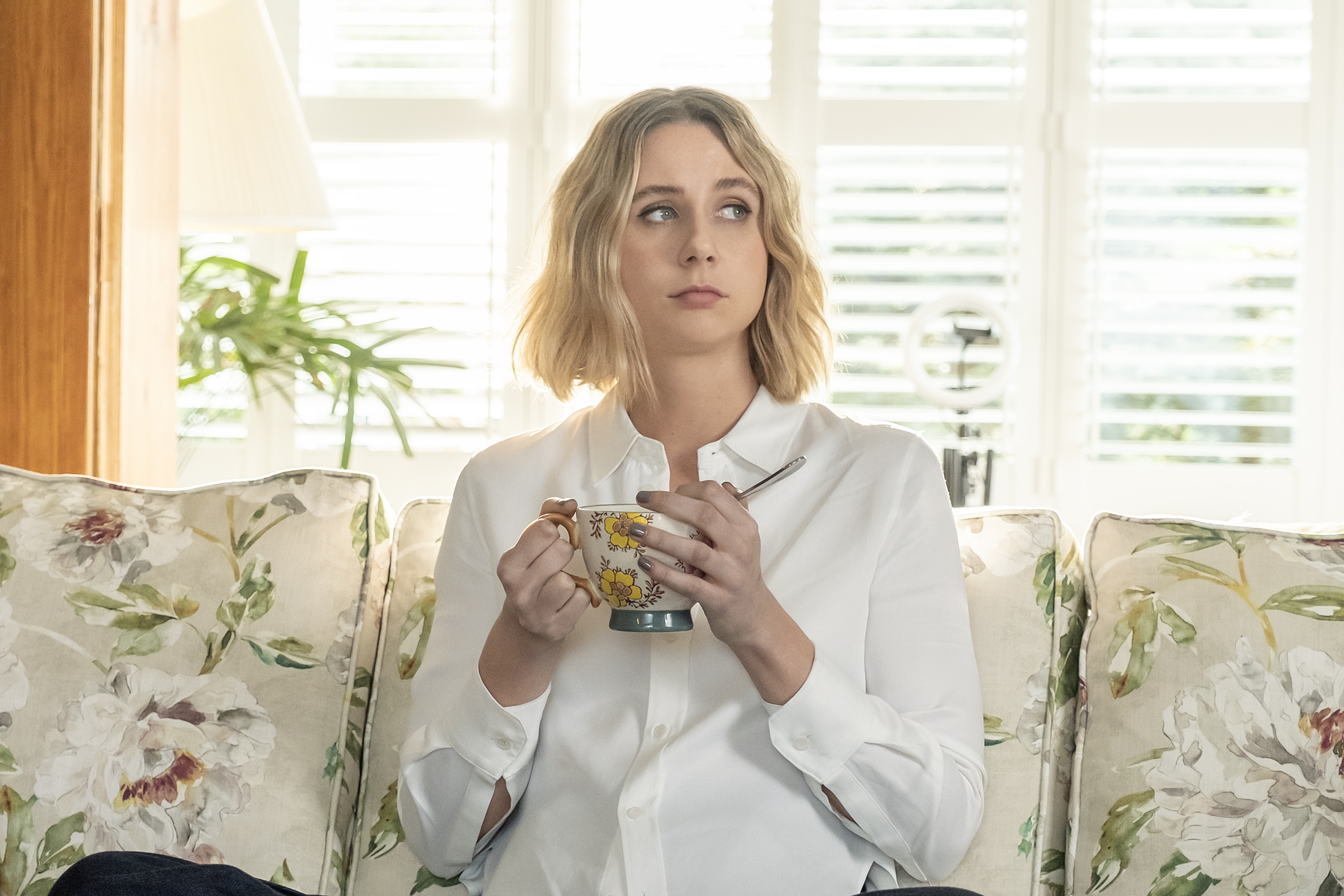 Lucy Freyer as Billie, holding a tea cup while sitting on a floral house in a living room, in 'Adults.'