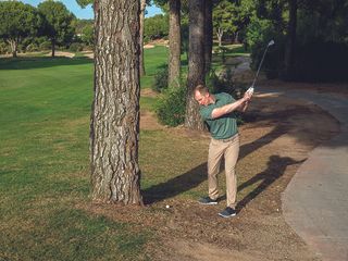 Golf Monthly Top 50 Coach John Howells hitting a shot from the base of a tree