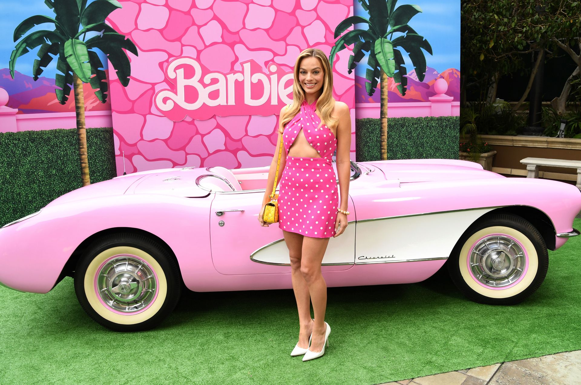 Margot Robbie in all pink posing in front of a pink convertible
