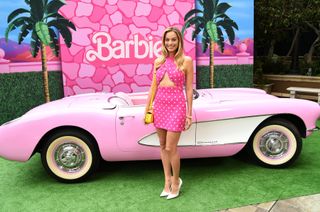 Margot Robbie in all pink posing in front of a pink convertible