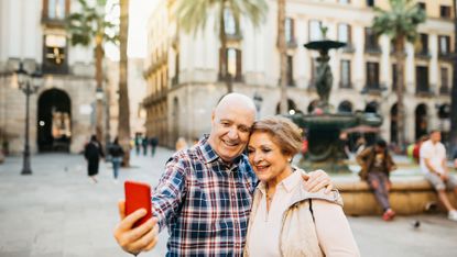 Cheerful senior couple taking a selfie in front of a fountain in Barcelona, Spain