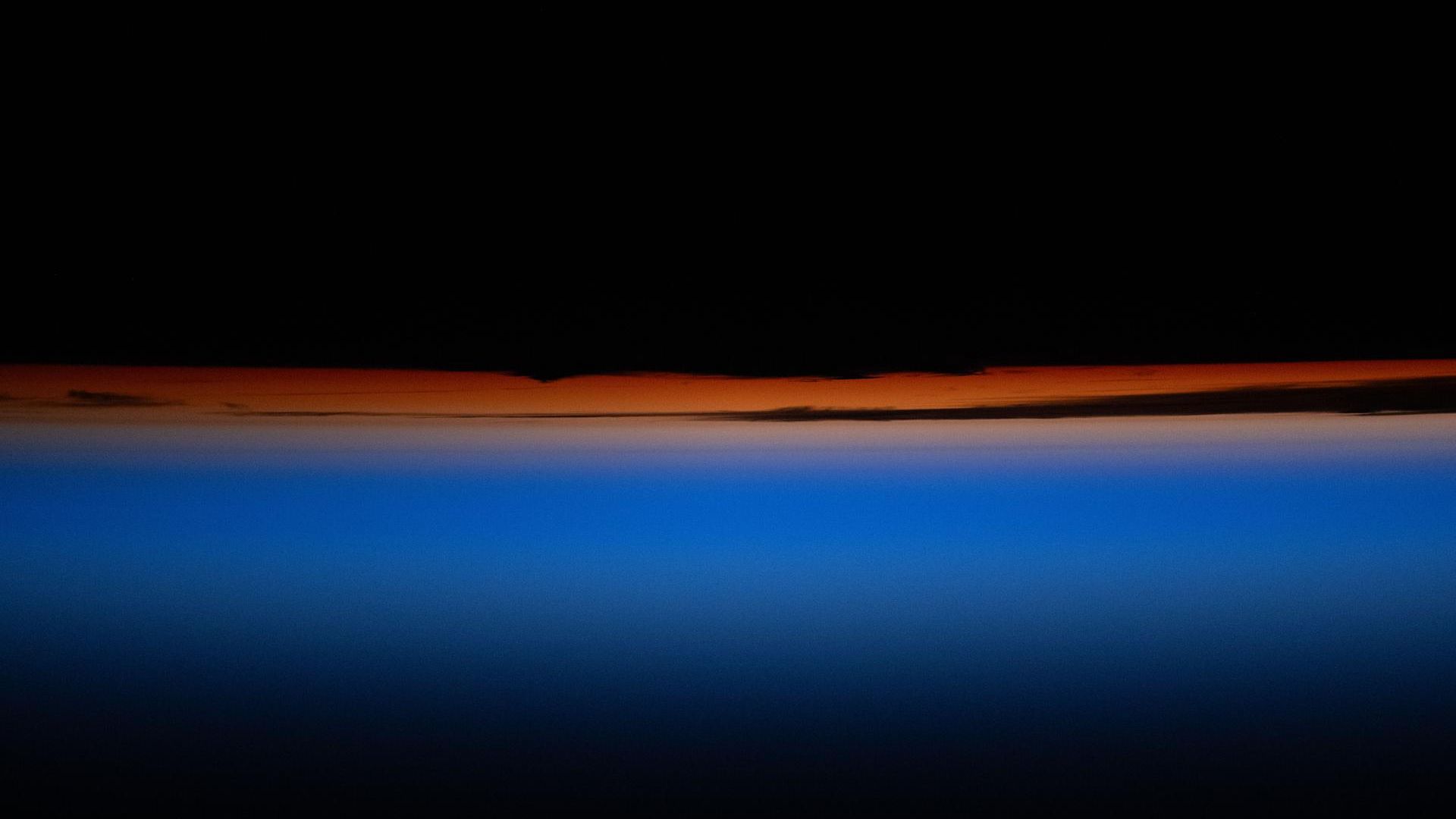 the top portion of the image is black followed by a bright red and orange band of color which blends into an ombre of blue into black at the bottom of the image. 