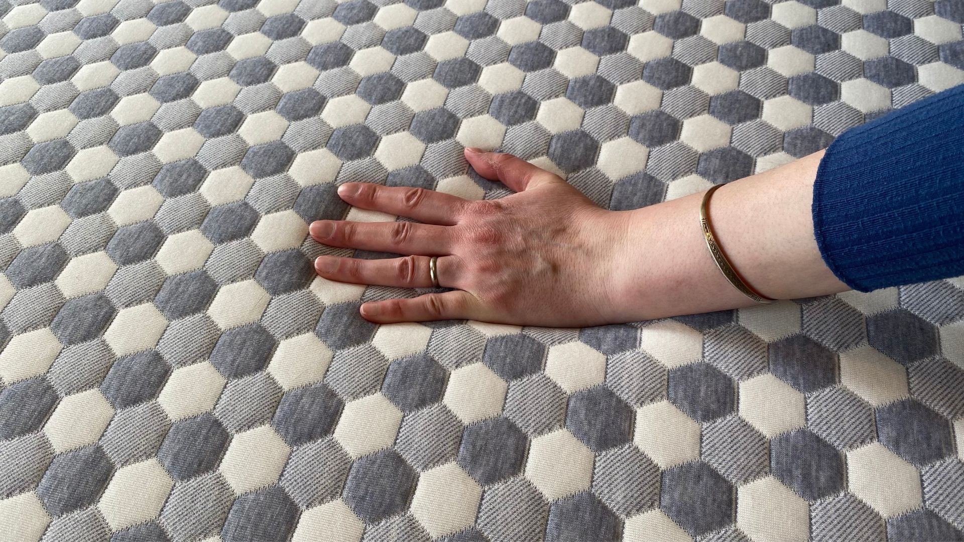 A woman places her hand on the cover of the Otty Firm Hybrid mattress to see how cool it is