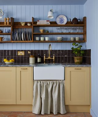 yellow and blue kitchen with wood paneling, open shelving and a traditional sink skirt