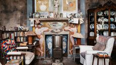 A richly ornate artist studio is filled with yellowed books, furniture, postcards, ephemera, and china porcelain kept in an antique cupboard and decorated with handpainted figurative murals.