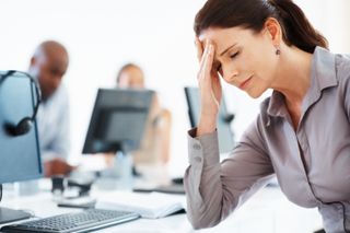 A woman looks stressed at work, while colleagues sit in the background.