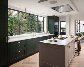 Designing a modern kitchen illustrated in a forest green scheme with wooden flooring, a taupe kitchen island and white countertops.