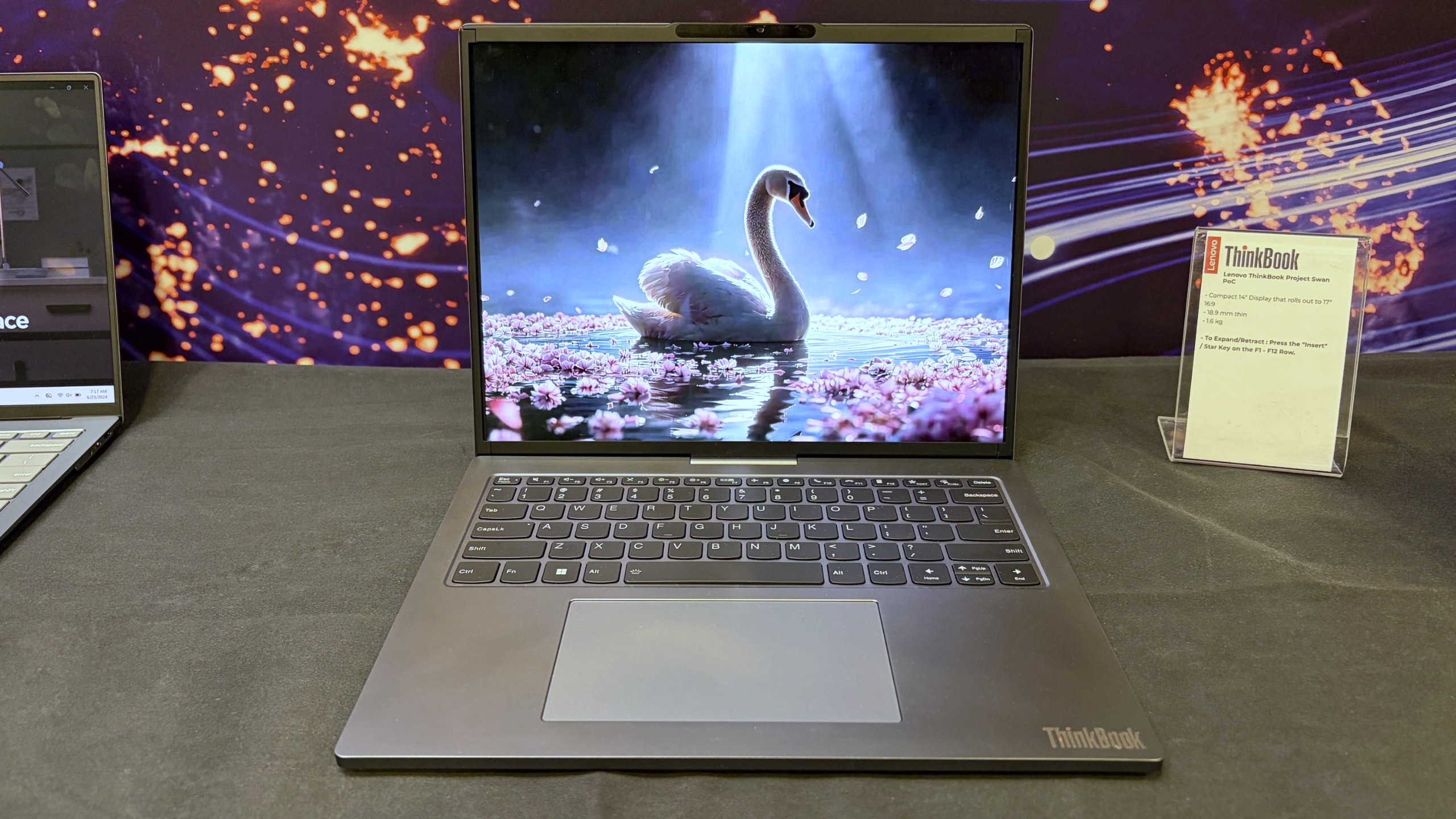 Lenovo ThinkBook Project Swan laptop on display, showing a vibrant swan with folded wings on a blue, starry lake scene at a tech exhibit.