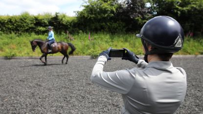 Person on the ground filming rider on horse in background for AI horse training