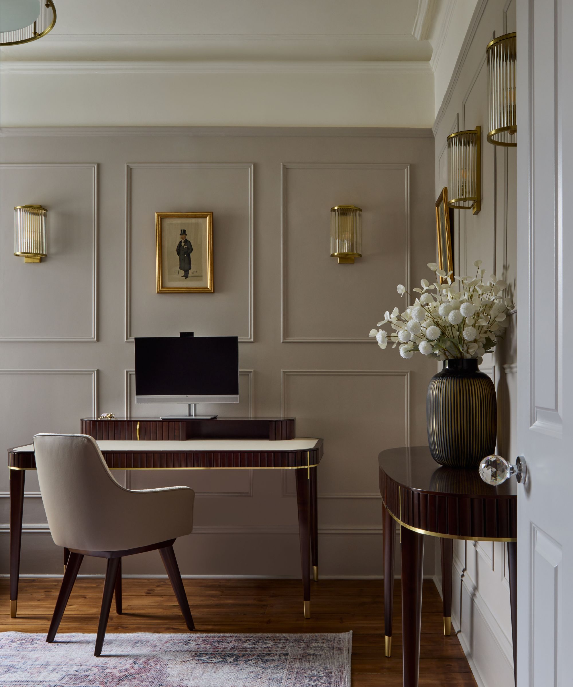 Home office with Elephant's Breath by Farrow &amp;amp; Ball painted walls, wall panelling, a dark wooden desk with a velvet grey desk chair and a matching wooden console table with a vase of flowers.
