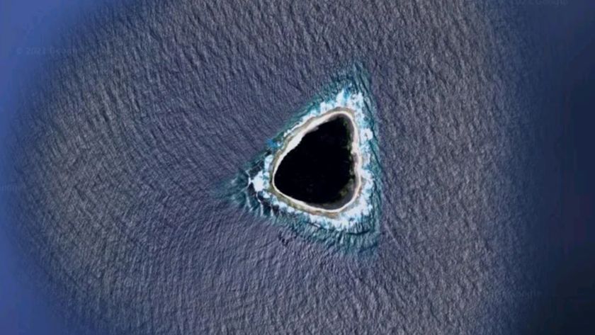 An aerial photo of a roughly triangular island in the sea, which looks almost completely black