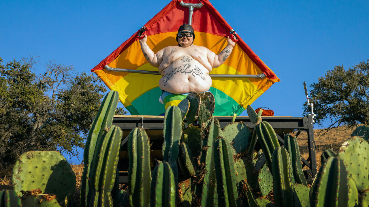 New Jackass cast member Zach Holmes is shirtless and wearing a kite, perched above cacti in an image from Jackass 4.5, one of the best Netflix comedies