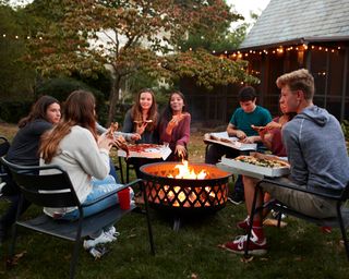 friends sit round a fire pit eating pizza
