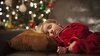 A kid sleeps on the sofa with a Christmas tree in the background