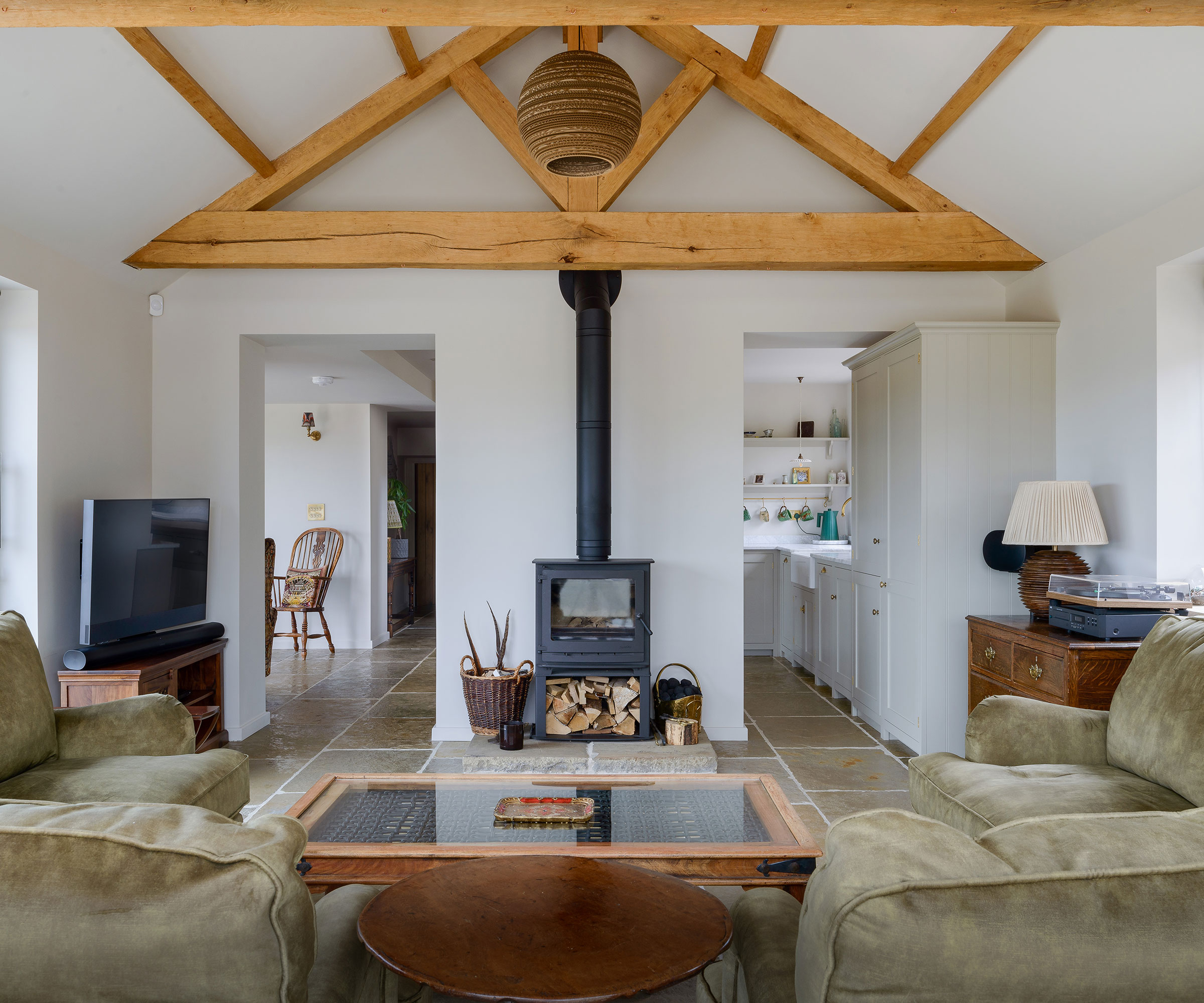 open-plan living and kitchen space with vaulted ceilings, exposed oak beams and a woodburning stove
