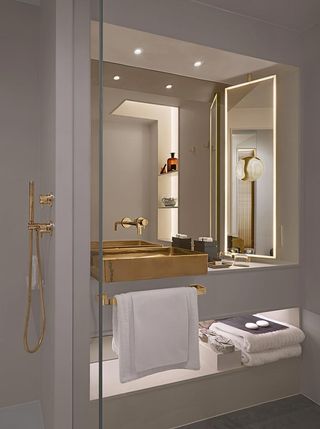 A bathroom in the Nobu Hotel Shoreditch. All white bathroom, with an open shower, a gold bathroom sink, and faucets.