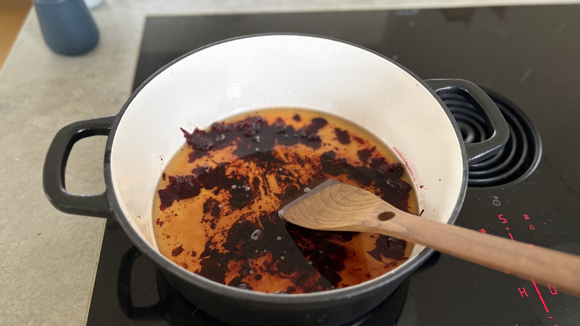 A stage of cleaning a burnt cast iron casserole dish on a hob