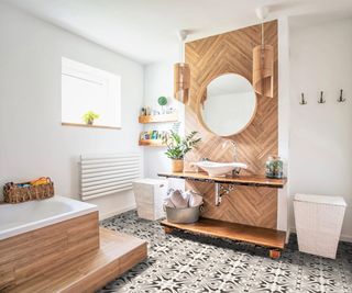 bathroom with wooden clad wall and wooden effect pendant lights hanging either side of round mirror above white sink on counter top