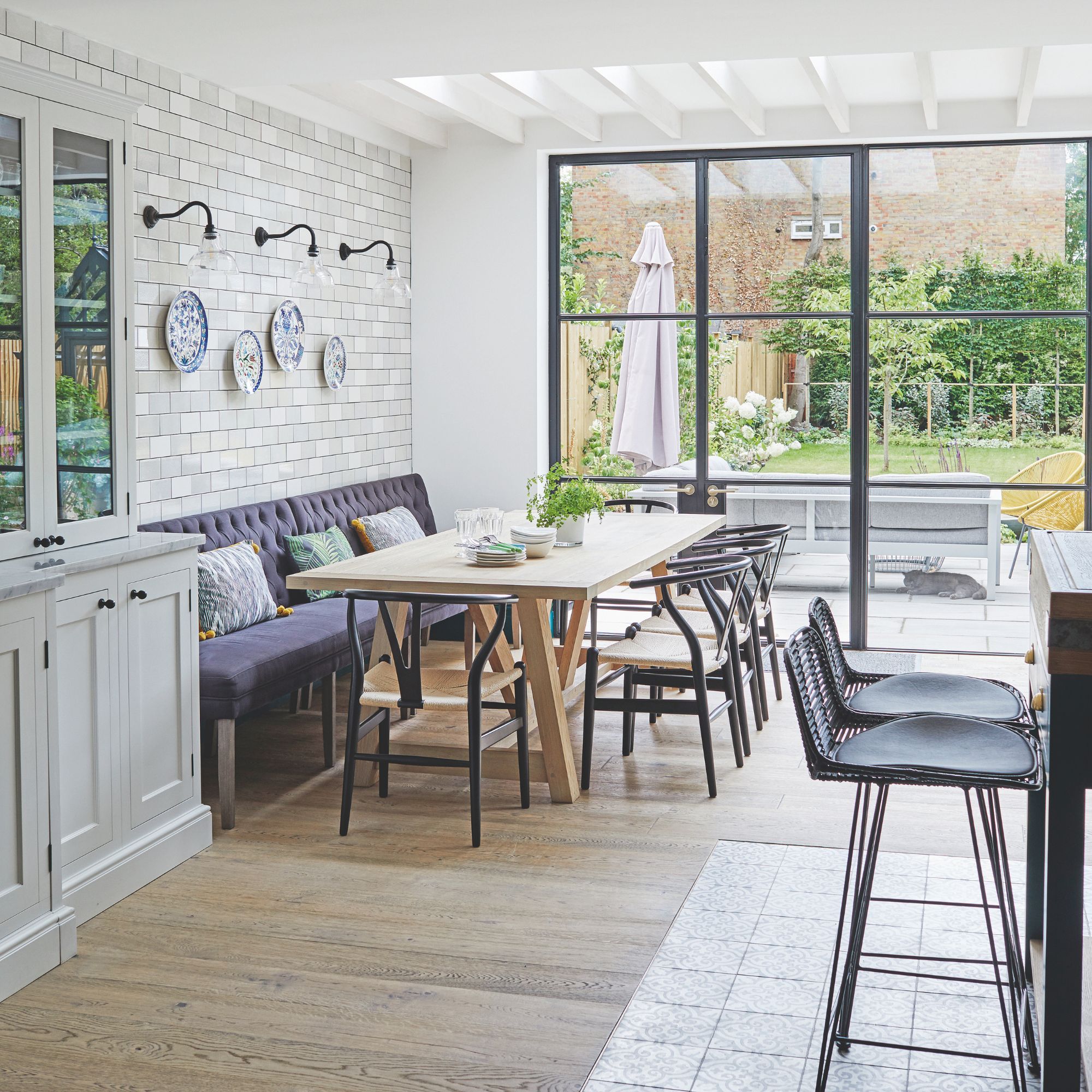 Kitchen diner area with a large dining room table and a mixture of bench and chair seats, with doors looking out onto the garden