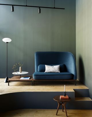 Green wallpapered corner with deep blue sofa, freestanding floor lamp and small table