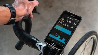 A smartphone fitted to handlebars with a TrainerRoad workout on screen