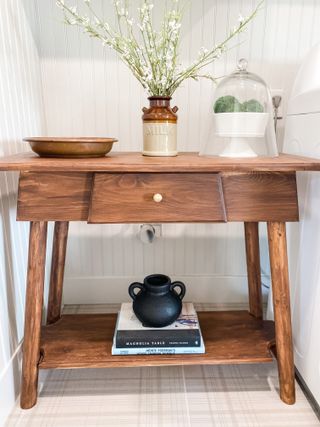 wooden console table with a vase and bowls and some books on the lower shelf