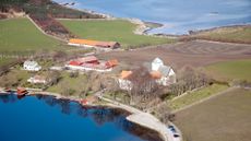 Island village on in Norway coast with small red, orange and white buildings surrounded by fields.