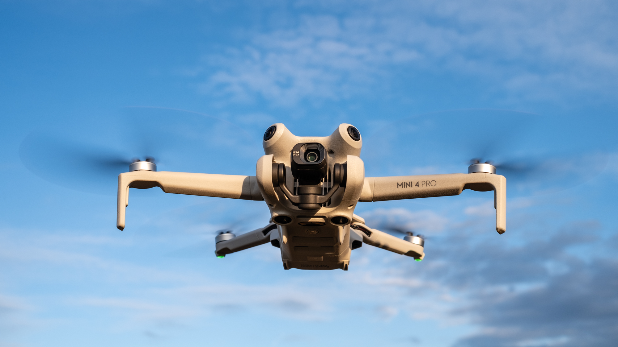 DJI Mini 4 Pro in flight against a blue sky with clouds
