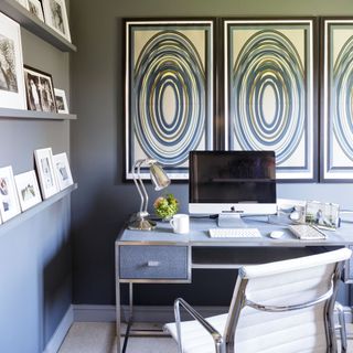 Green-grey home office with desk, paintings and art on picture rails