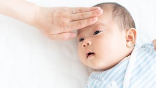 Mom holding hand to baby's forehead to check temperature.