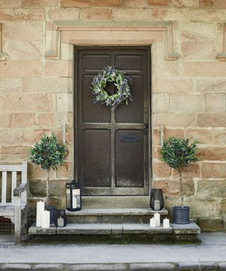 front door with faux wreath, 2 bay trees, steps with candles and lanterns