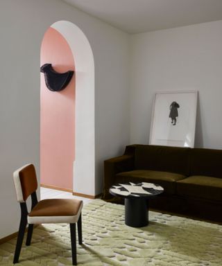 living space with light green rug, white walls and dark brown sofa with arched doorway leading into pink room