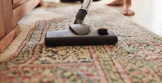 vacuuming a rug in a living room to show the first step for how to clean a rug at home