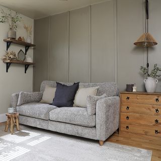 A living room with one wall covered in grey-painted panelling and with a light grey sofa in front of it