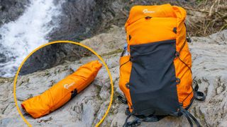 A Lowepro RunAbout Daypack in the field, one of the best camera backpacks, on a rocky surface in front of a waterfall