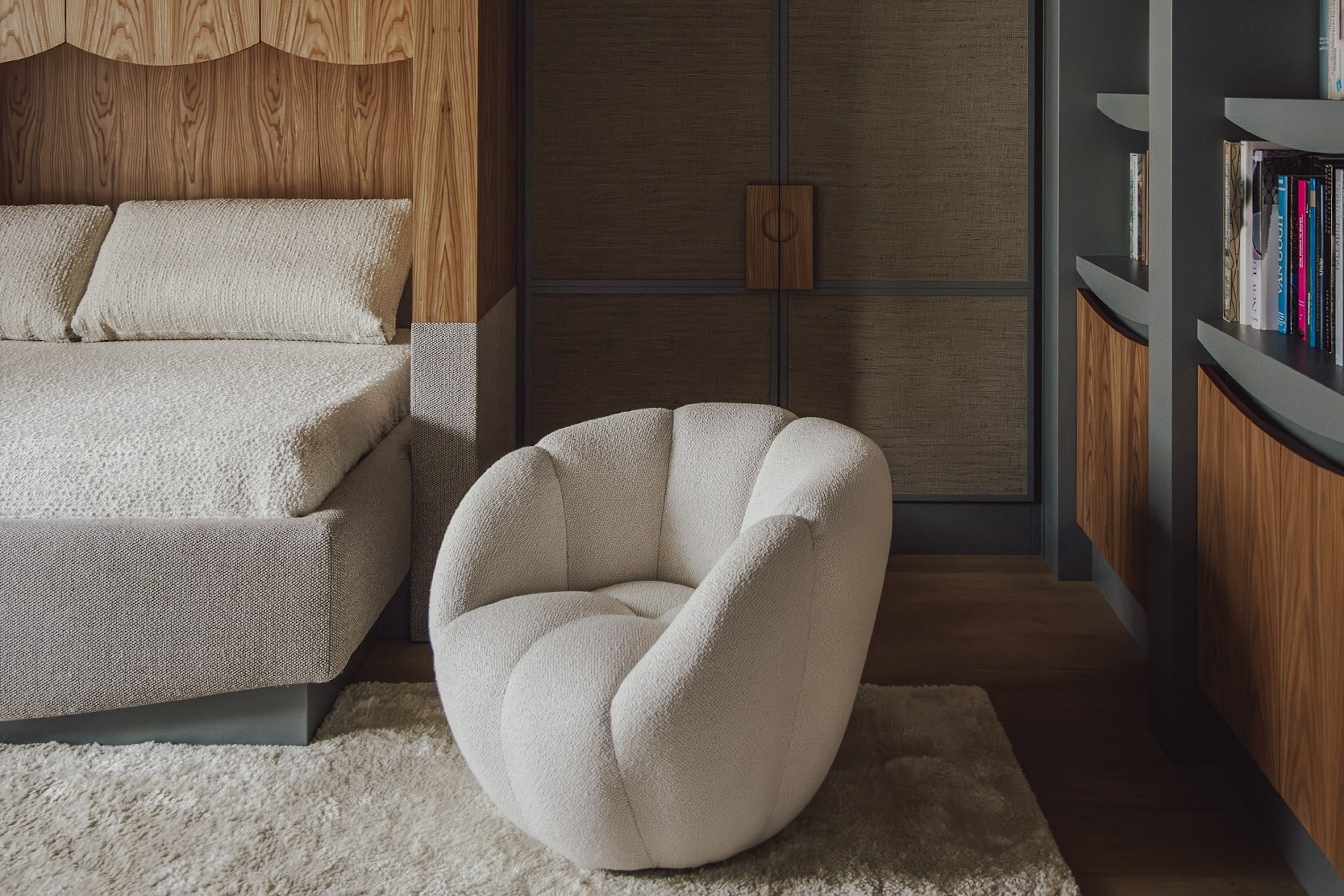 A contemporary bedroom with cream boucl&amp;eacute; bedding and upholstery and matching grainy wood bedframe, door handles, and drawers